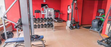 Ein Fitnessstudio mit roten Wänden, verschiedenen Trainingsgeräten und einer Holzzieldecke.