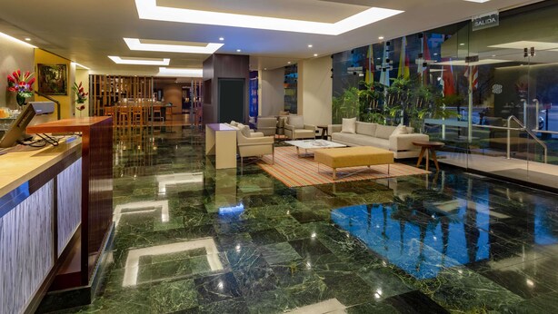 Un moderno vestíbulo de hotel con mostrador de recepción, zona de estar y pared de vidrio con vistas al exterior.