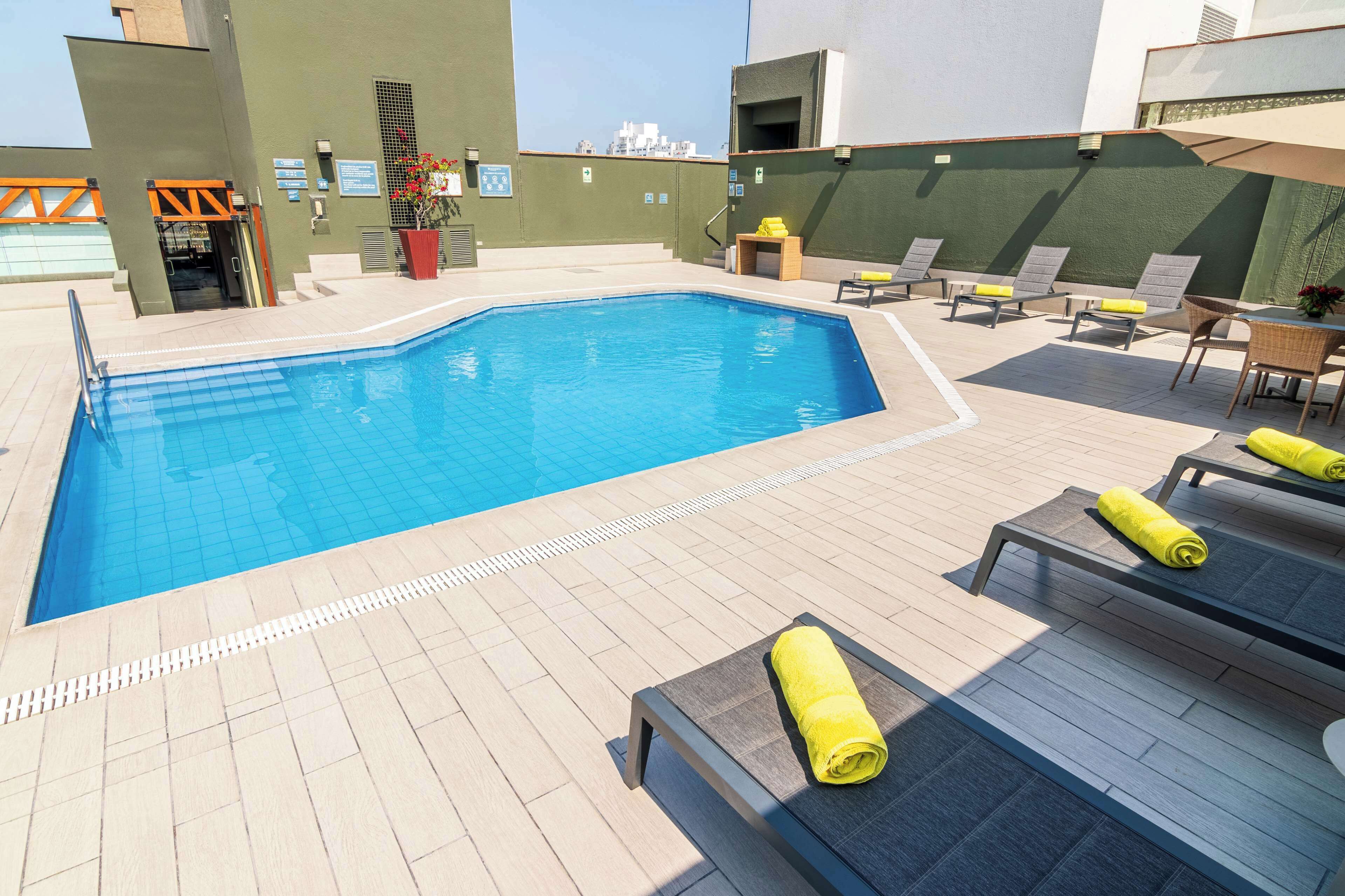 A swimming pool with lounge chairs and sun loungers, a potted plant, and a small table with a yellow towel.