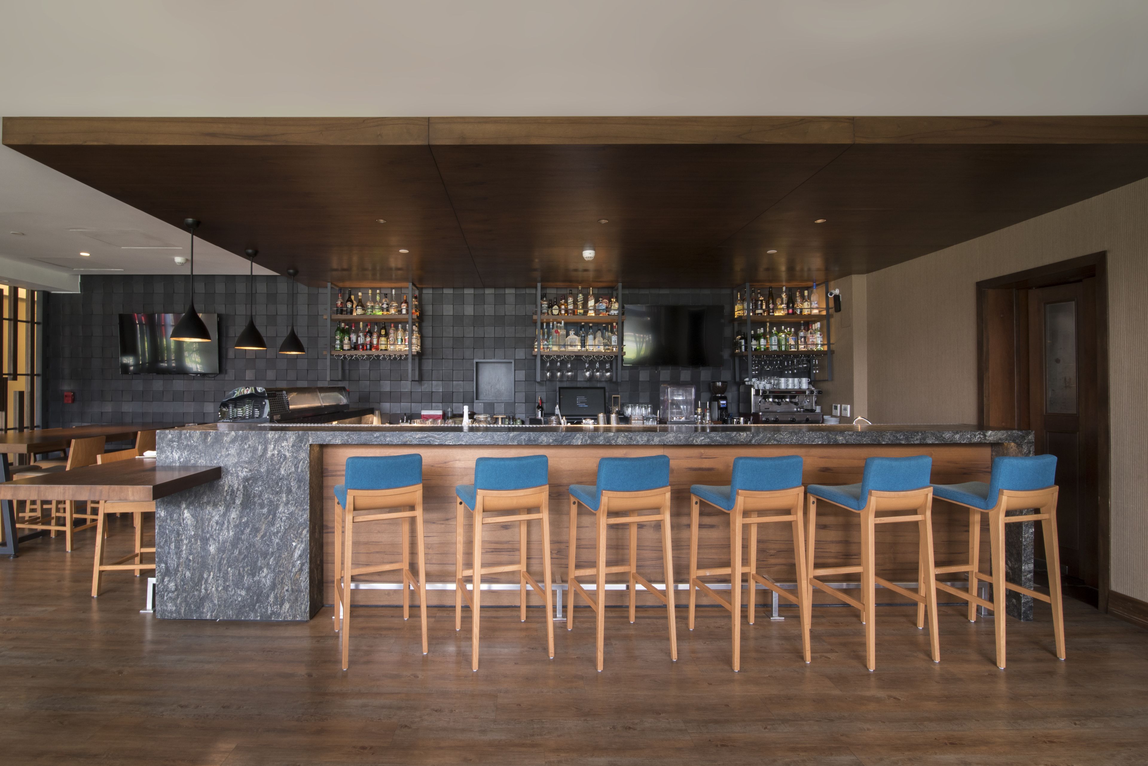 Angolo bar con bancone in marmo, sgabelli in legno e soffitto in legno scuro.
