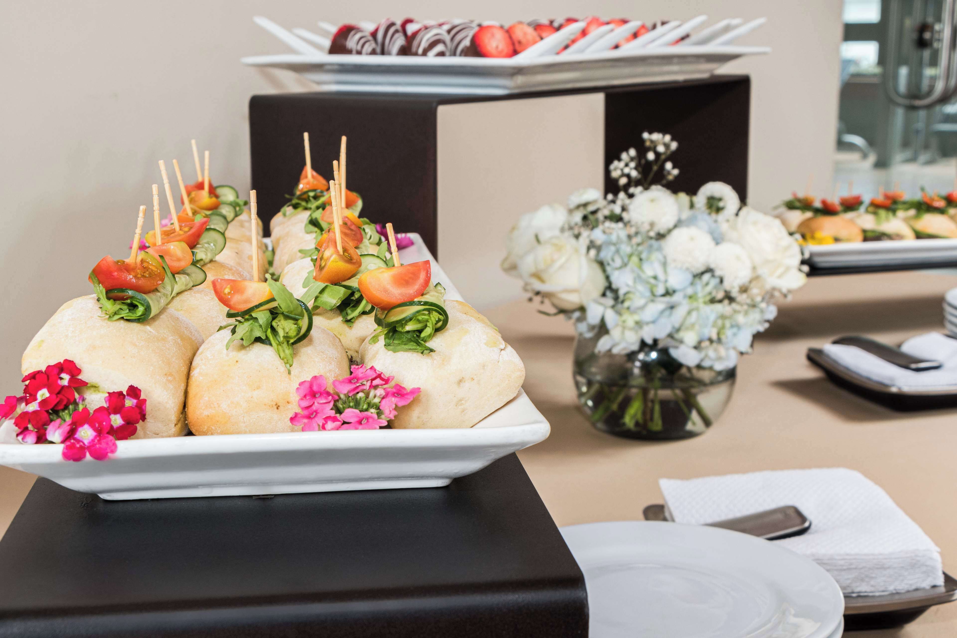 Une table de buffet proposant divers plats, notamment des légumes et des pâtisseries présentés sur des brochettes, ainsi qu'un vase rempli de fleurs.