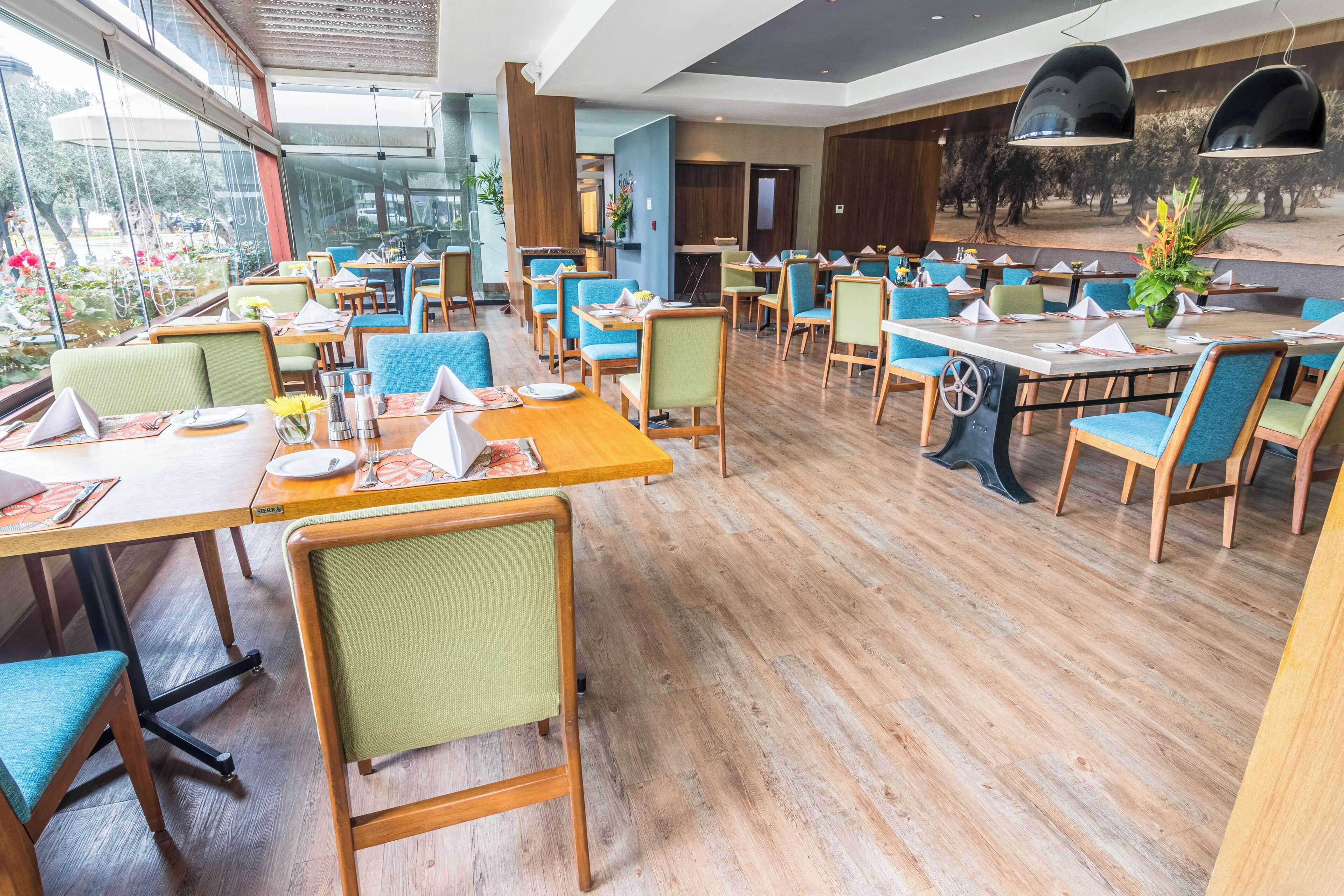 Un restaurante con mesas y sillas de madera, ventanas amplias y vistas al exterior.