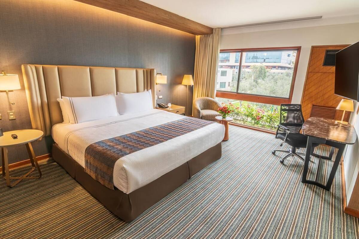 Quarto de hotel com uma cama grande, uma escrivaninha, uma cadeira, uma televisão e vista para o exterior.