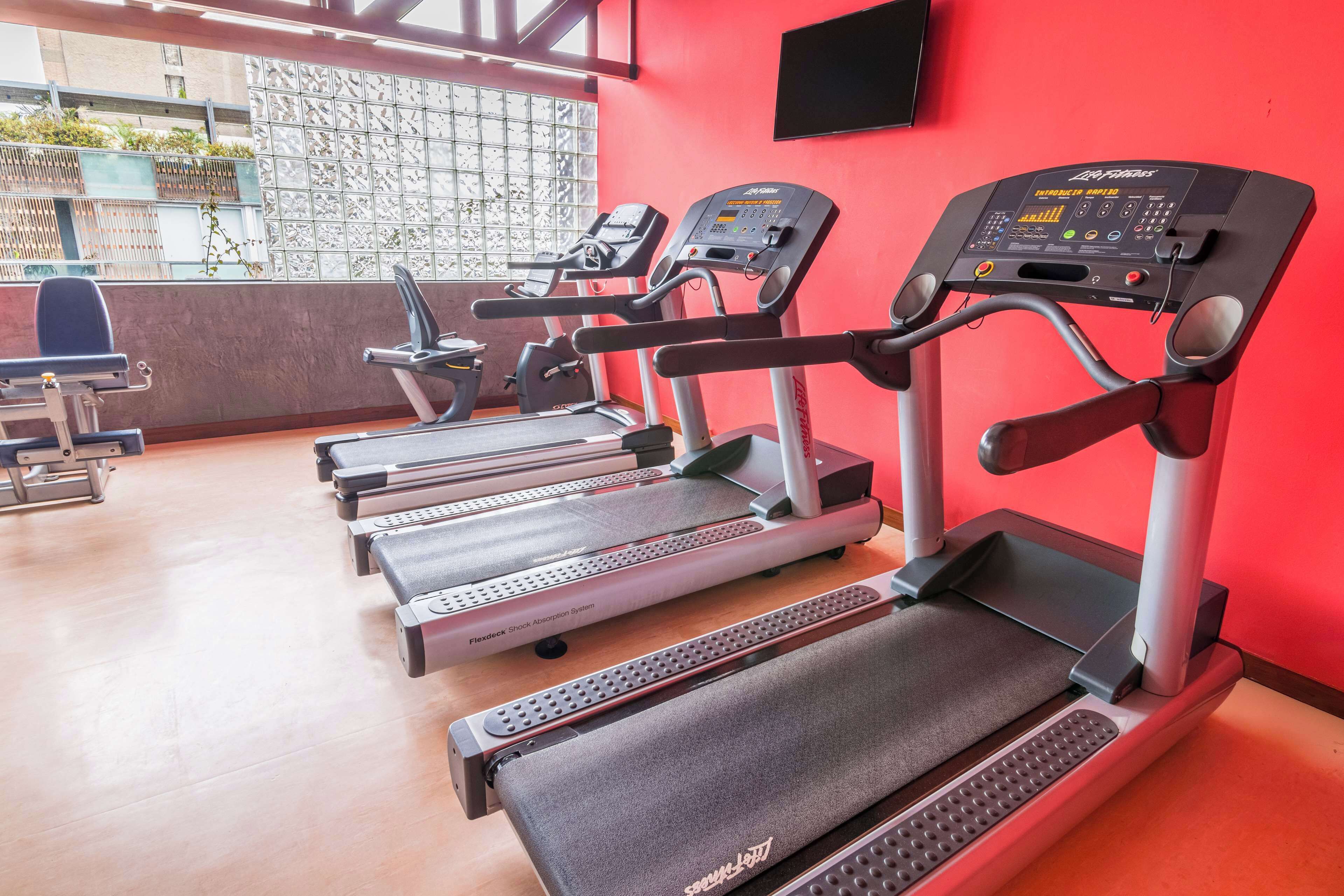 A gym with treadmills, exercise bikes, and a red wall.
