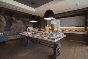 A modern breakfast buffet with a variety of food items and a seating area with a sofa and chairs. - Sonesta Hotel El Olivar Lima (Lima)