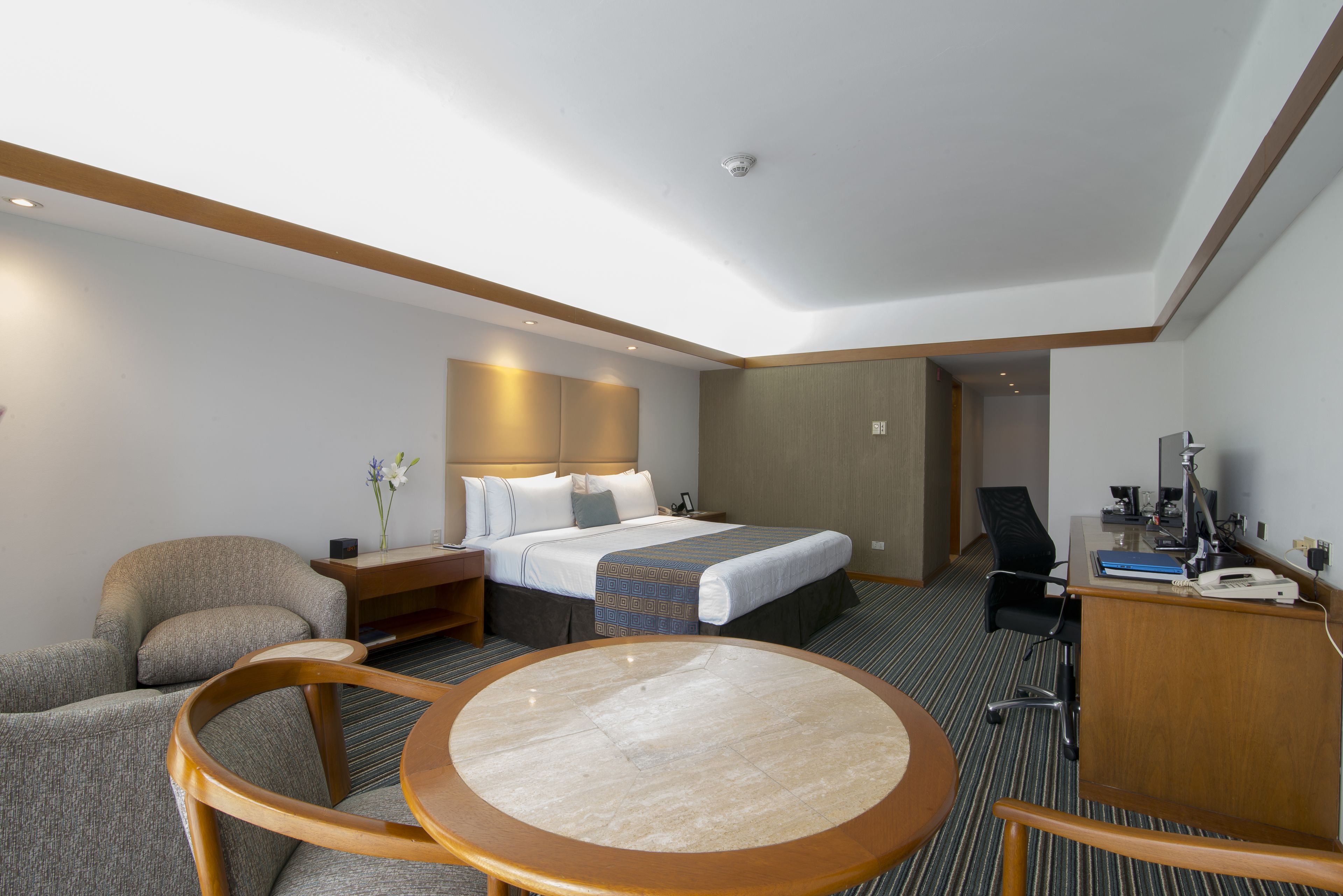 A hotel room with a bed, a desk, a chair, a round table, and a small desk lamp.