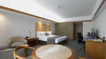 Een hotelkamer met een bed, een bureau, een stoel, een ronde tafel en een kleine bureaulamp.