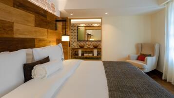 Habitación de hotel con una cama grande, cabecera de madera, un espejo, una silla y una mesita con lámpara.