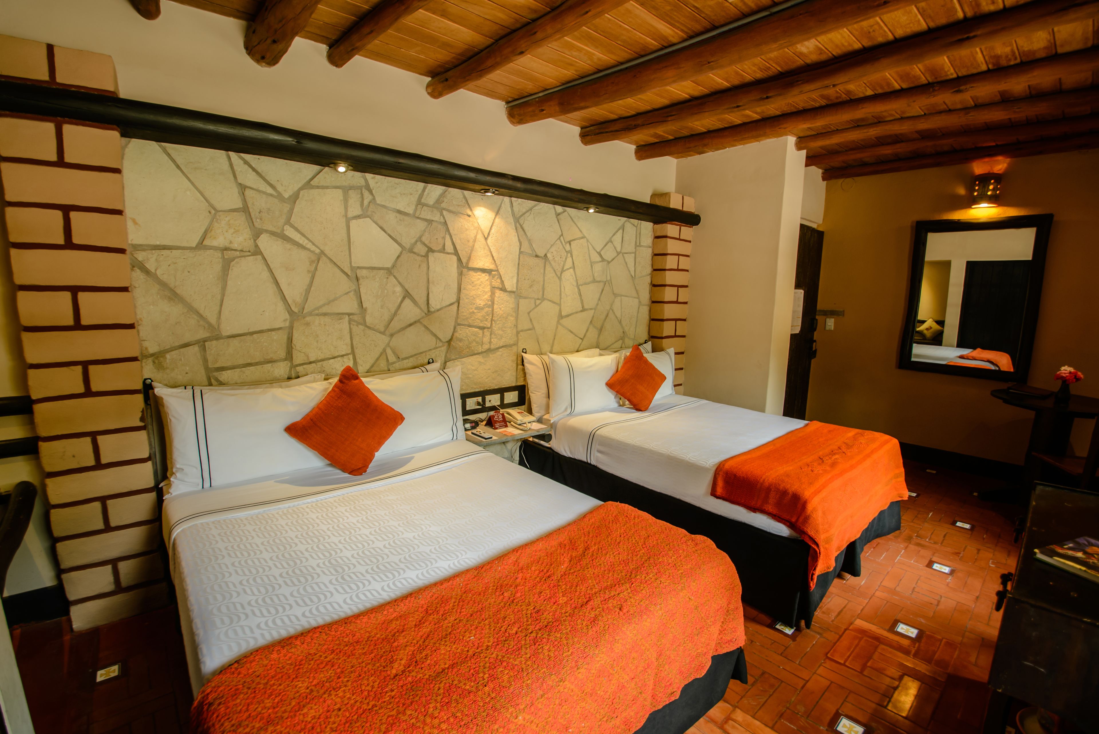 A hotel room with two beds, a stone wall, wooden ceiling beams, and a mirror on the wall.