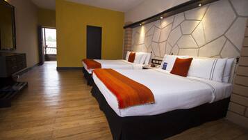 A hotel room with three beds, wooden flooring, a modern wall design, and a large mirror.