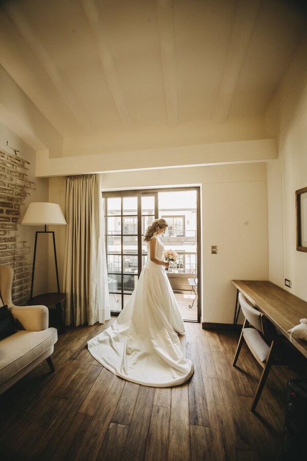 A room with a wooden floor, a sofa, a lamp, a table, and a window with curtains.