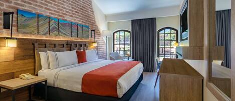 A modern hotel room with a brick wall, a large bed, a desk, and a TV.