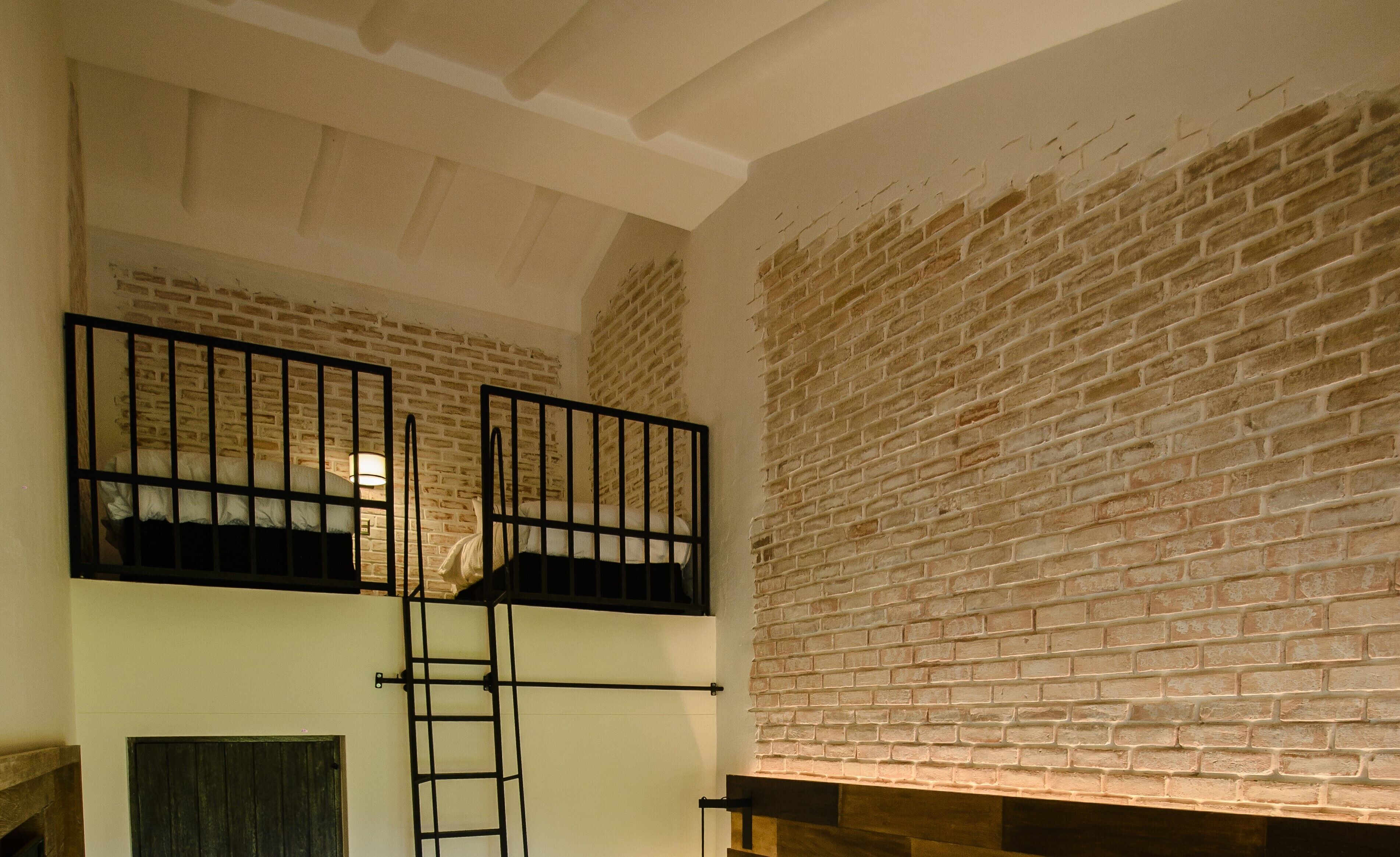 A room with a brick wall and a loft area with a ladder.