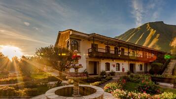 Traditional architecture meets serene surroundings, with a central entrance, balcony, and beautifully maintained garden.