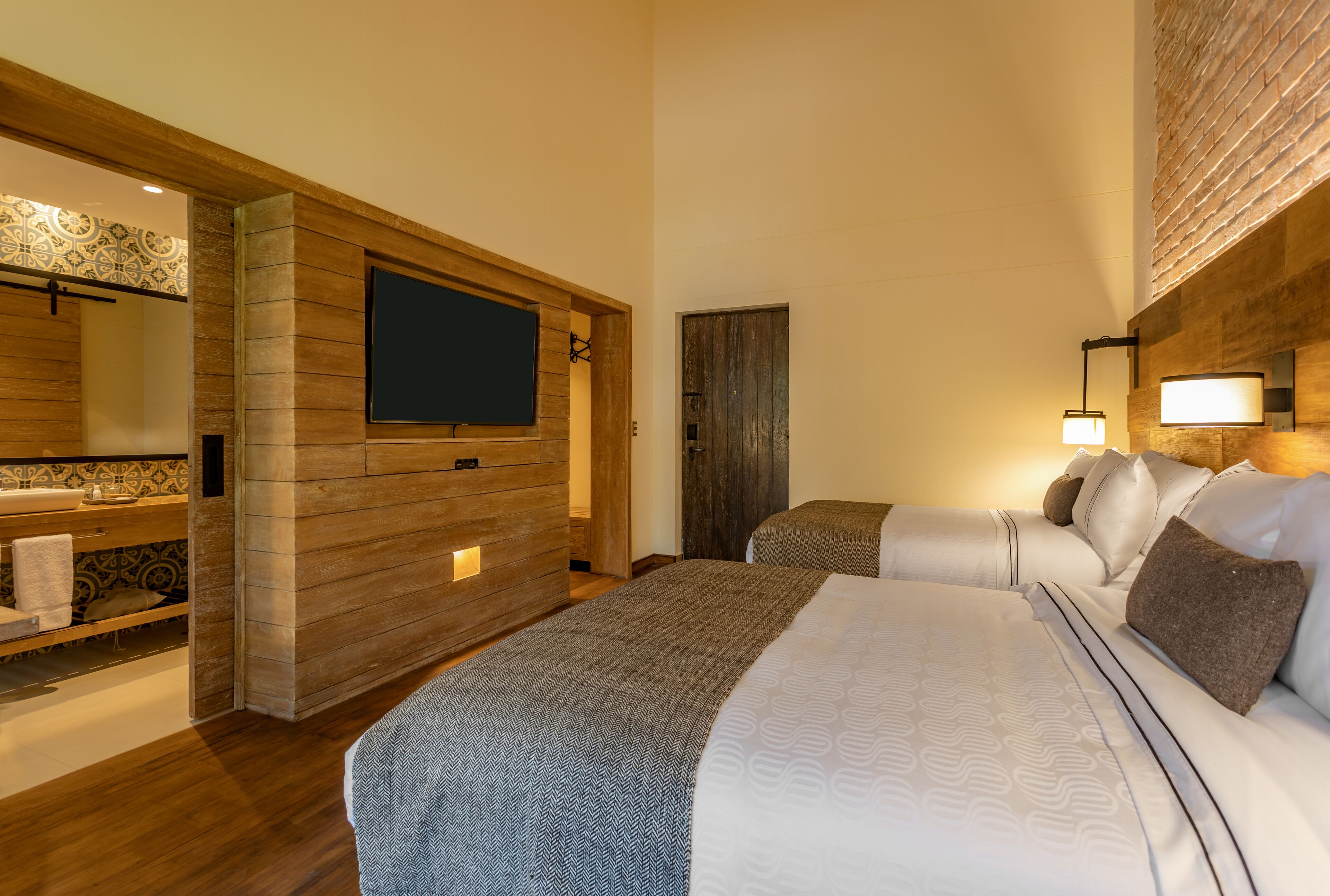 Habitación de hotel con una cama grande, un panel de pared de madera, un televisor, un baño con salpicadero de azulejos estampados y una mesita de noche.