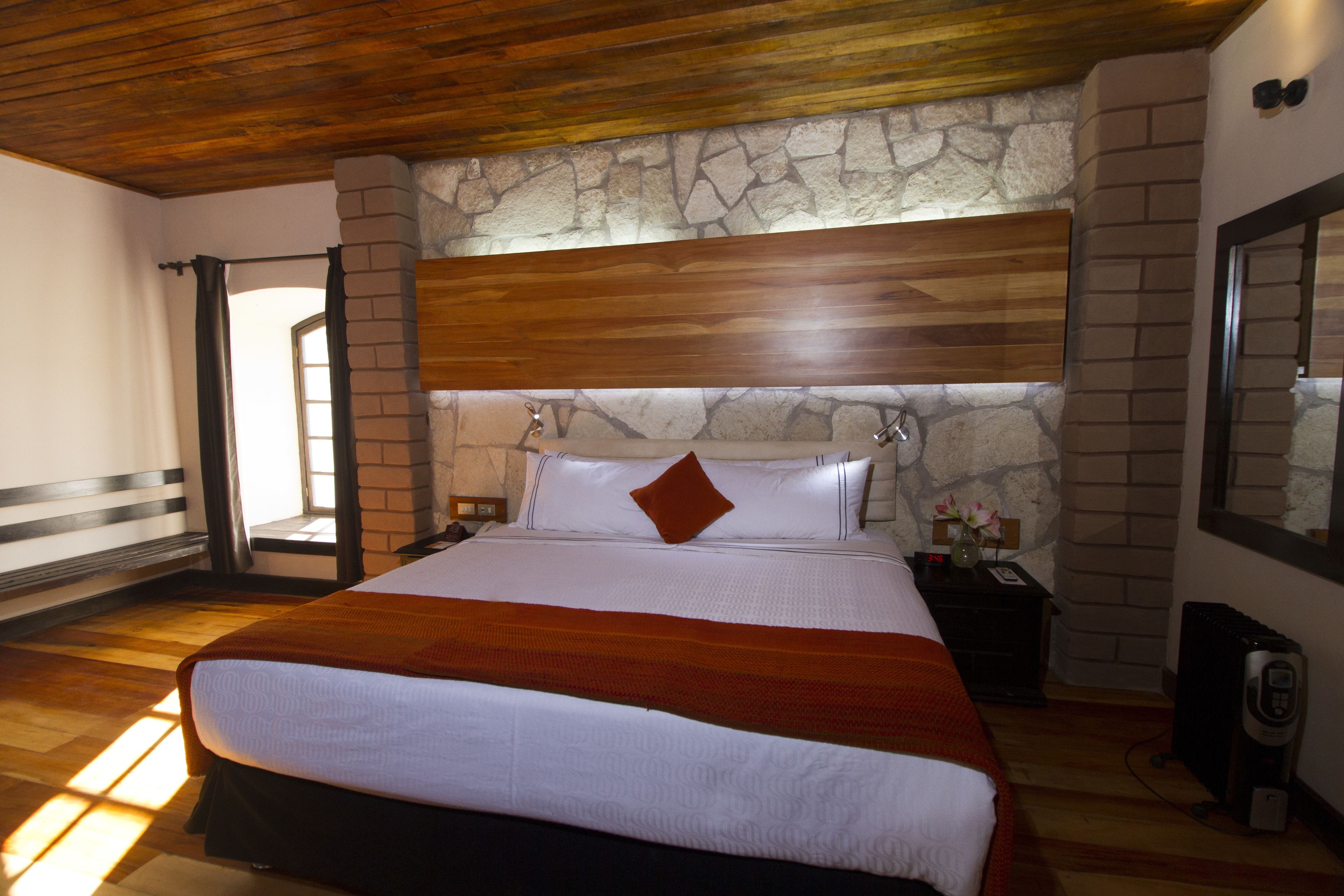 A spacious bedroom with a large bed, wooden headboard, stone wall, and a nightstand with a lamp.