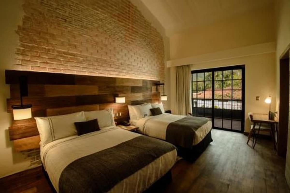 A hotel room with two beds, a brick wall, and a view through a glass door.