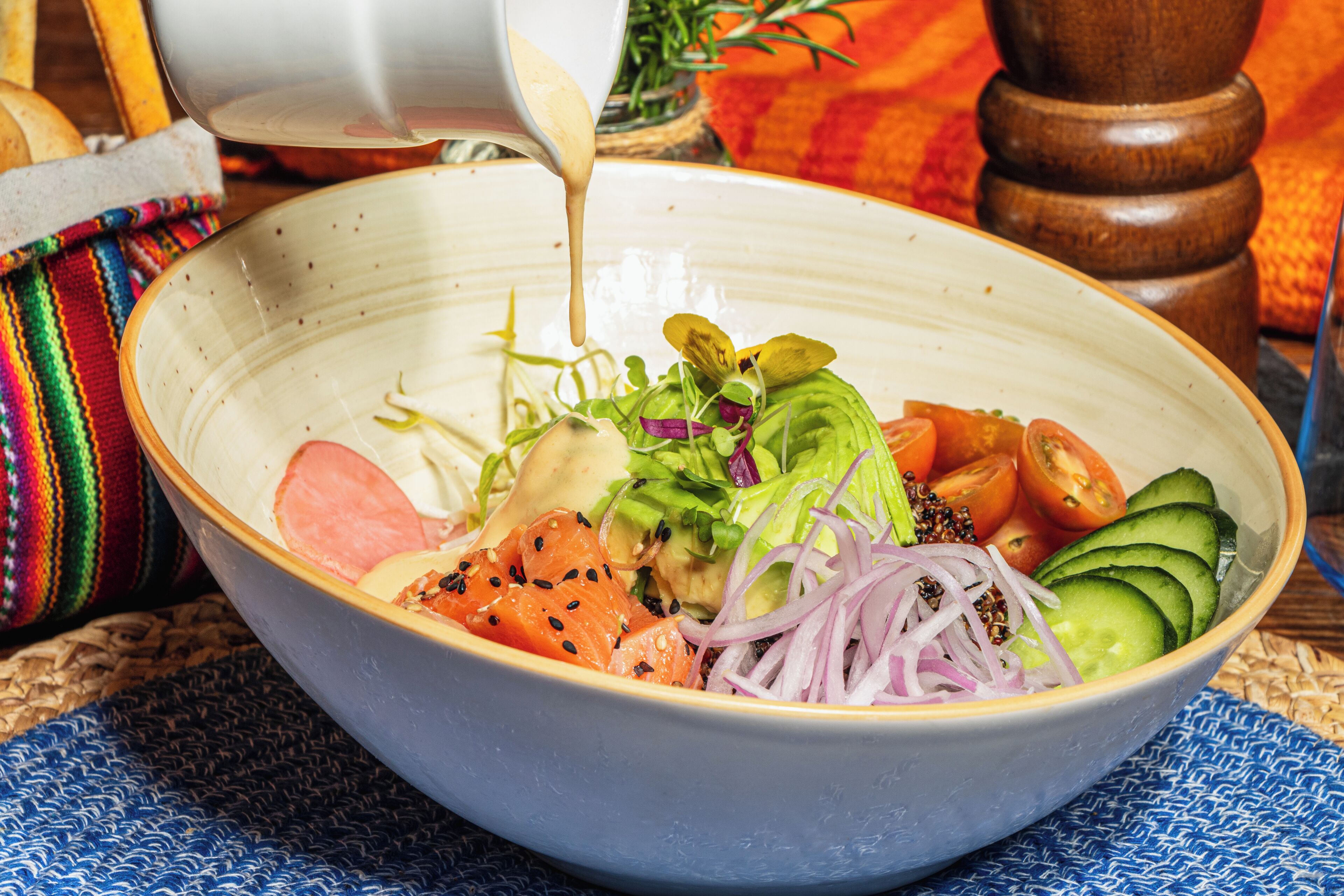 Un saladier rempli de salade, sur lequel on verse divers ingrédients.