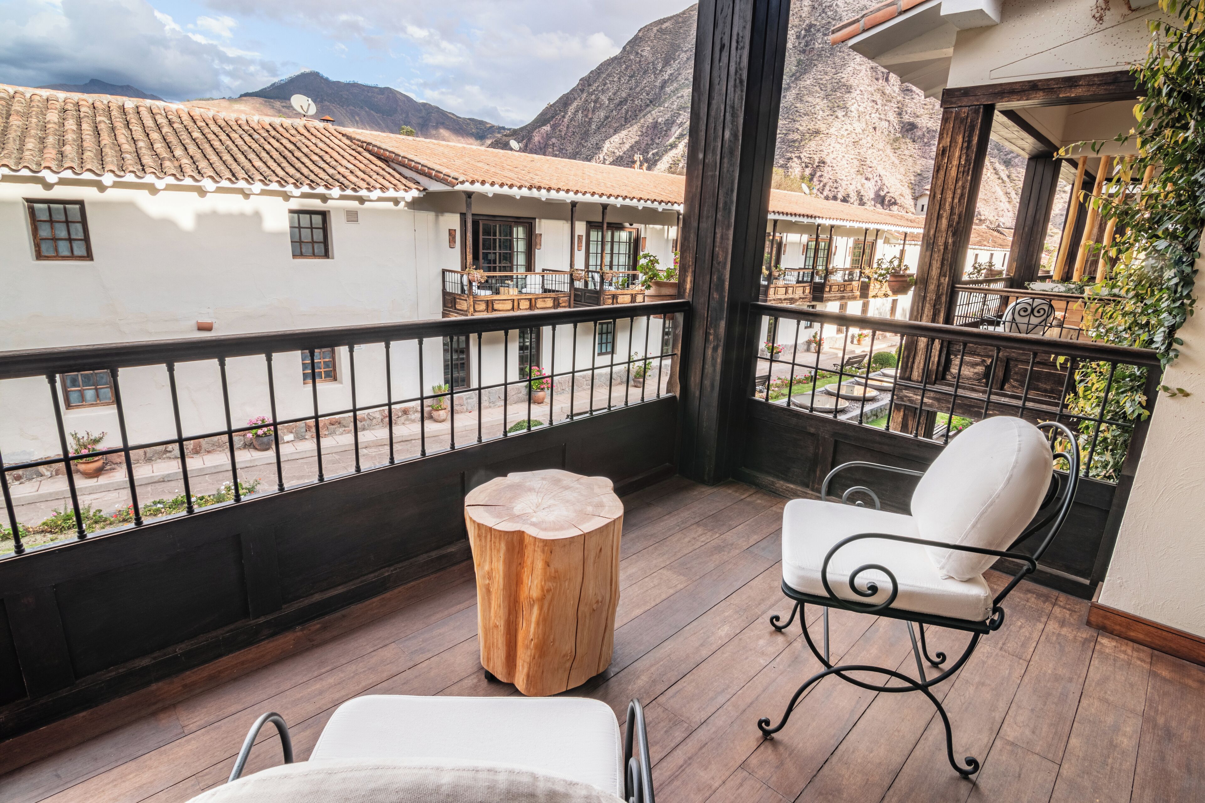 Un balcon avec un tabouret en bois, une chaise blanche rembourrée et une chaise à ossature métallique.