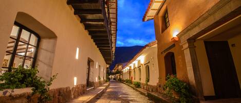 A narrow cobblestone street flanked by buildings with arched windows and outdoor lighting.