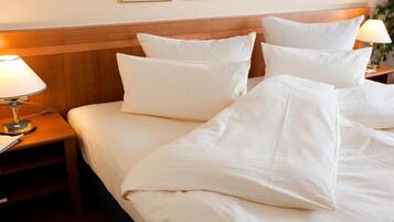 A neatly made bed with white linens and pillows, a wooden headboard, and a bedside table with a lamp.
