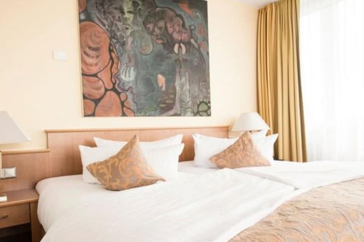 A hotel room with a large bed, a nightstand, a lamp, and a painting on the wall.