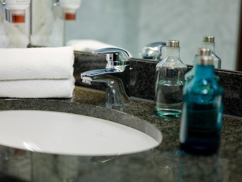 A bathroom sink with a chrome faucet, a white countertop, and a glass bottle of blue liquid.