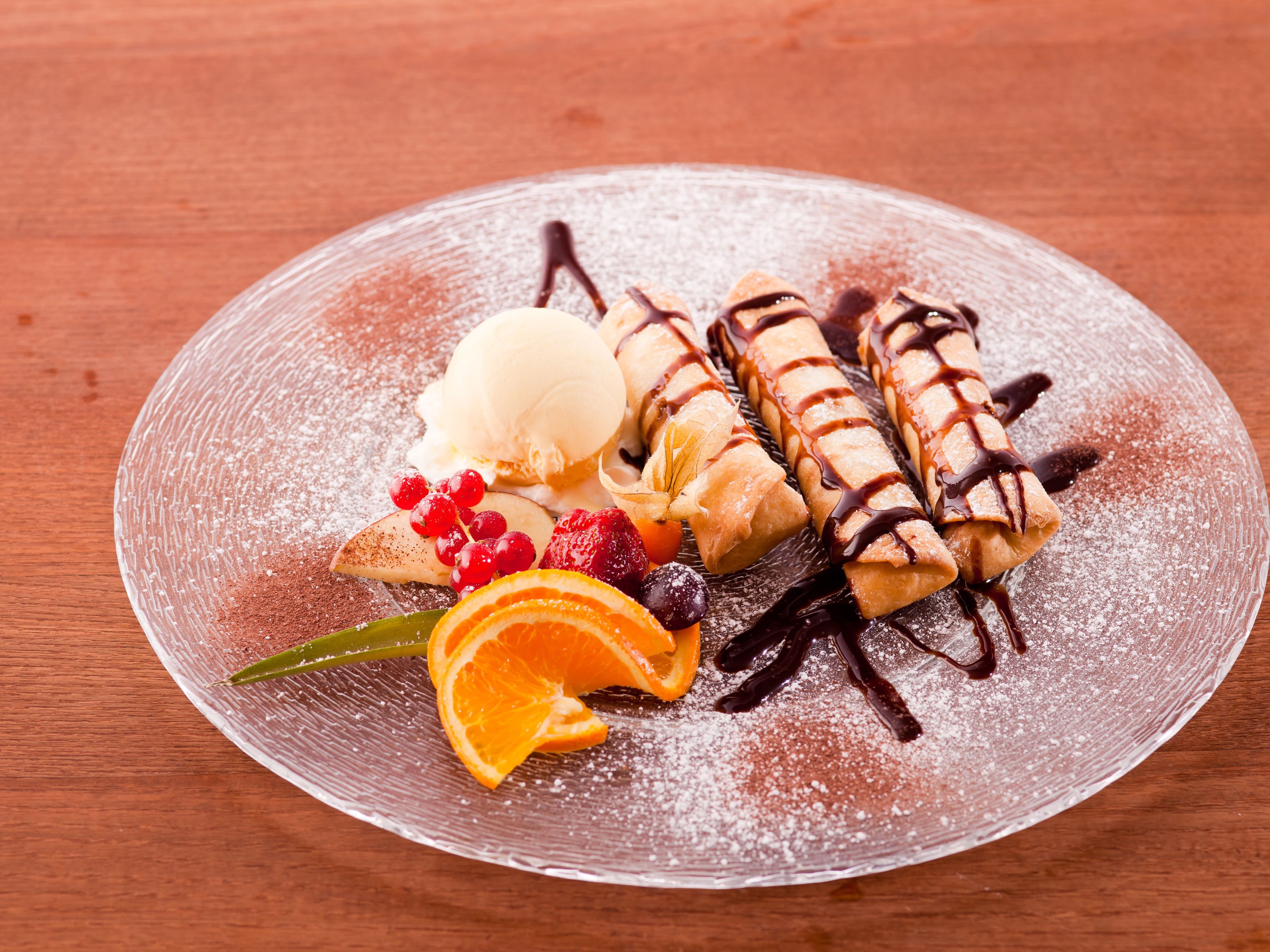 Un plato de postre con pastelería enrollada, helado y guarniciones de fruta.