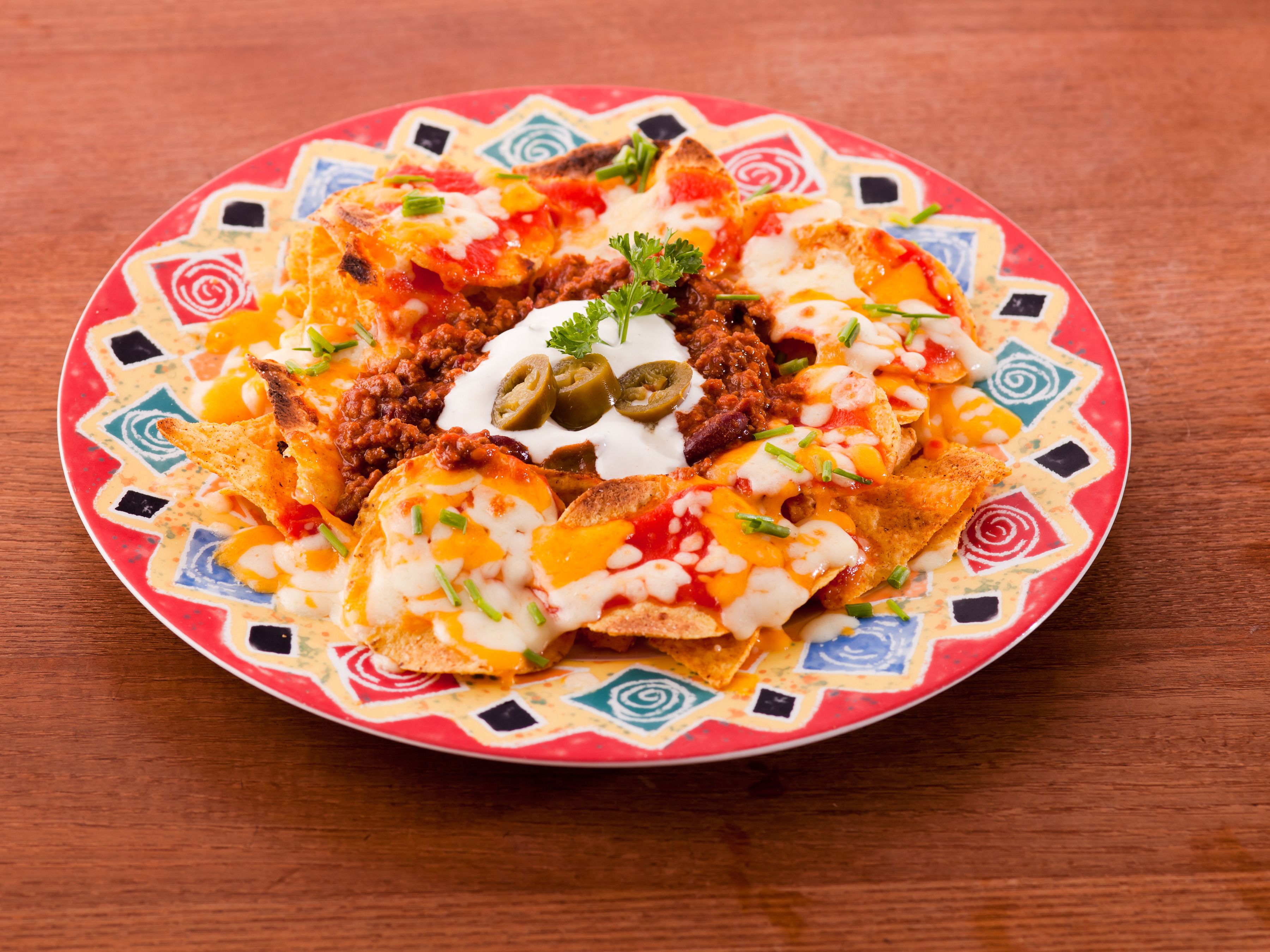 Une assiette de nachos garnis de fromage, de piments jalapeños et de crème aigre, le tout présenté sur une assiette aux motifs colorés.