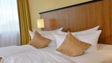 A neatly made bed with white linens and two decorative pillows, a wooden headboard, and a bedside lamp.