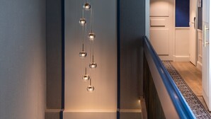 A modern interior with a staircase, a hanging light fixture, and a view of a kitchen area. - Hotel Cambon (Paris)