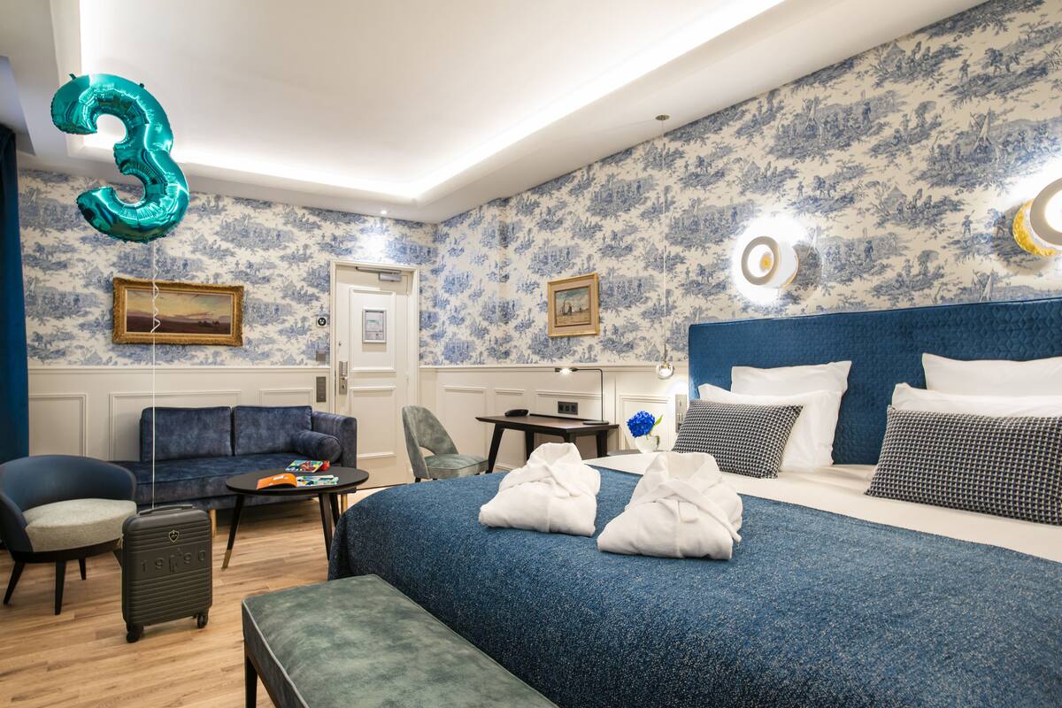 Hotelkamer met een groot bed, een bank, een bureau en een stoel. Er is een ballon met het cijfer 3 en een foto aan de muur.