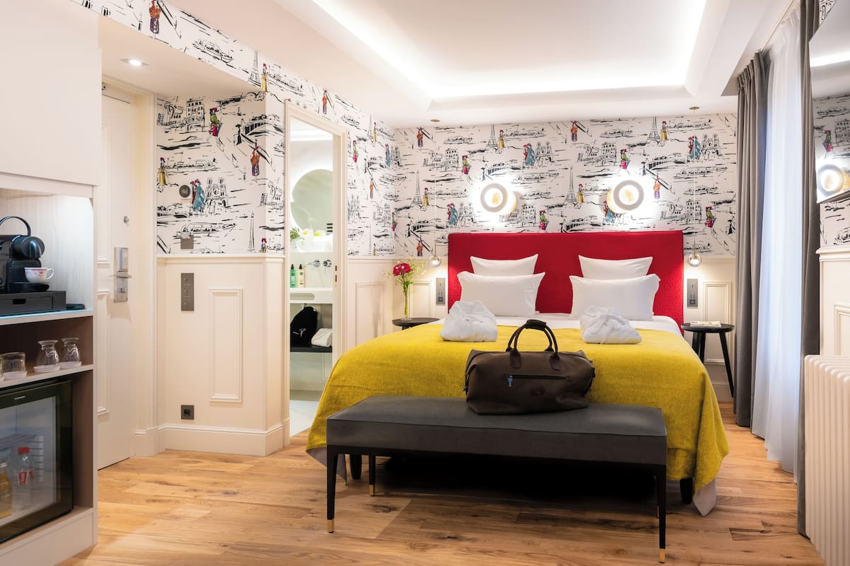 Een moderne hotelkamer met een rode hoofdbord, een gele sprei en een bankje met een handtas.