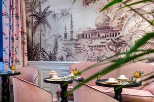 A restaurant with pink upholstered seating, black tables, and a mural of a mosque and palm trees.