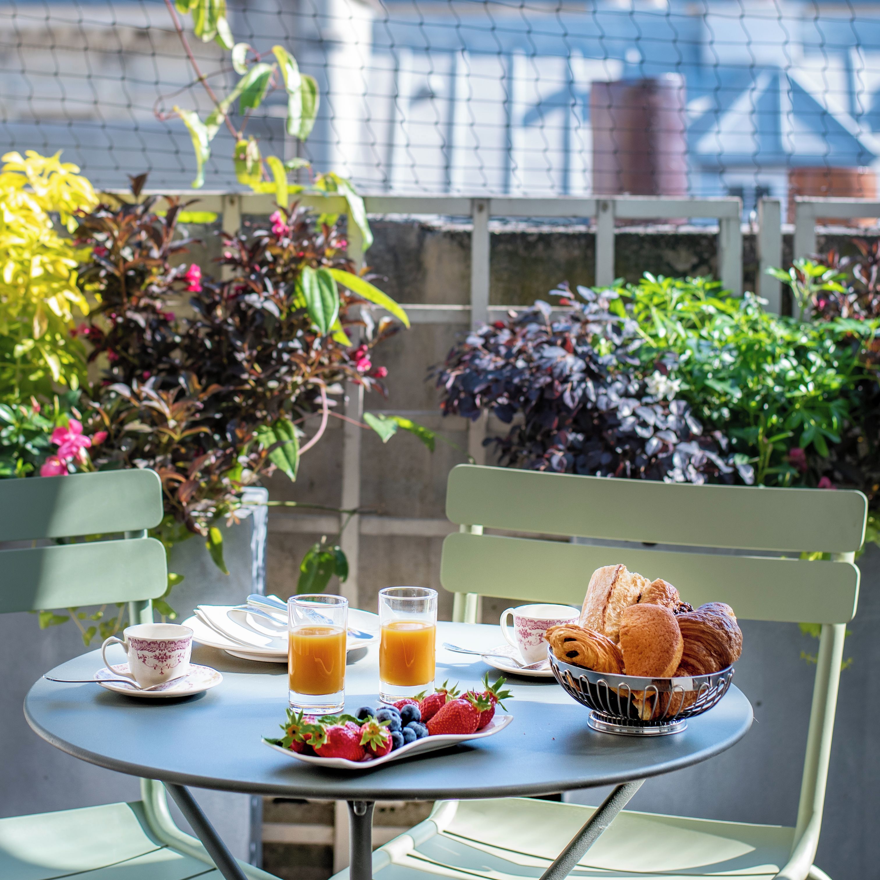 A table set with breakfast items including croissants, fruit, and orange juice, with chairs and a view of greenery.