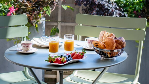 A table with breakfast items including croissants, fruit, and orange juice, set on a balcony with chairs and potted plants in the background. - Hotel Cambon (Paris)