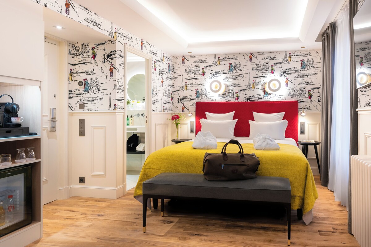 A modern hotel room with a red headboard, a yellow bedspread, and a bench with a handbag.