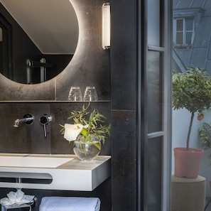 A modern bathroom with a large mirror, a white sink, and a vase with a white flower. - Hotel Cambon (Paris)