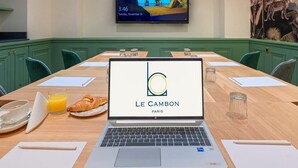 A conference room with a laptop displaying 'LE CAMBON PARIS' logo, a wooden table with breakfast items, and a TV on the wall. - Hotel Cambon (Paris)