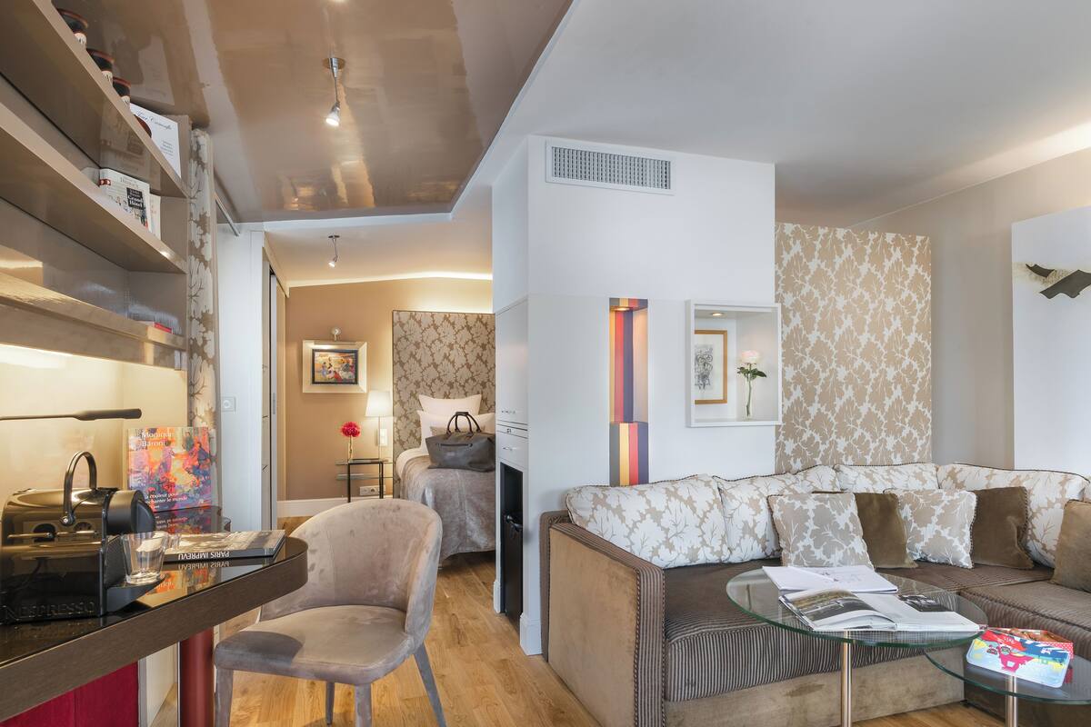 Een moderne woonkamer met een bank, een glazen bijzettafeltje en een stoel. Er is een boekenkast met boeken en een waterkoker op tafel.