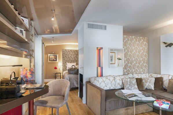 A modern living room with a sofa, a glass coffee table, and a chair. There is a bookshelf with books and a kettle on the table. - Hotel Cambon (Paris)