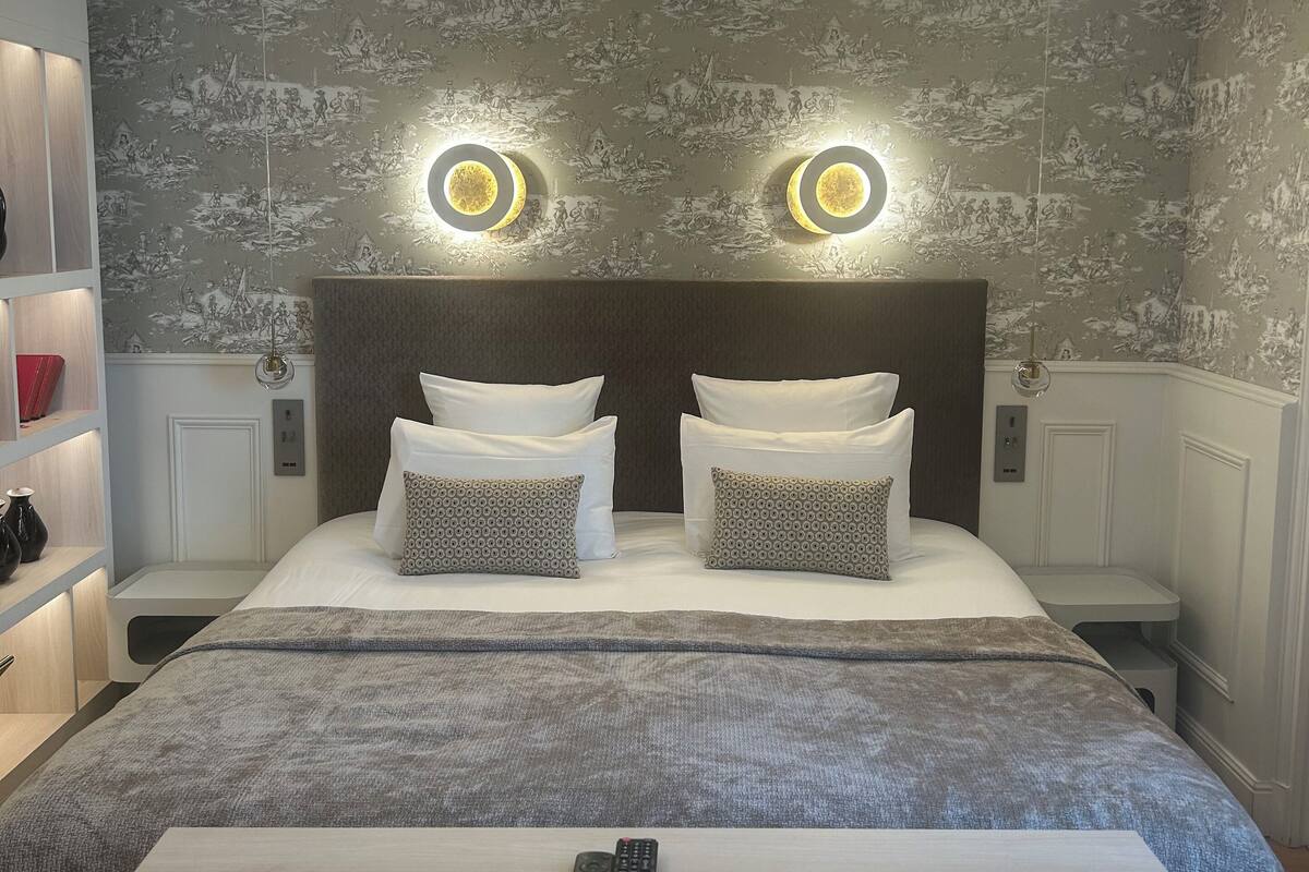 Een moderne slaapkamer met een groot bed, twee nachtkastjes en een bijzetmeubel.