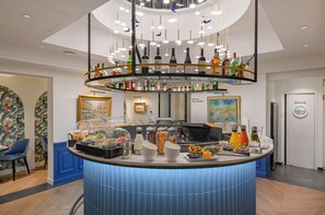 A modern bar area with a variety of liquor bottles, a fruit display, and a counter with a blue design. - Hotel Cambon (Paris)