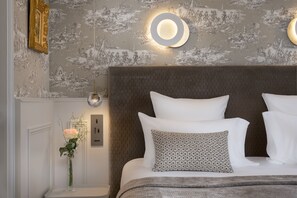 A bedroom with a large bed, a nightstand, a wall-mounted light, and a floral arrangement.