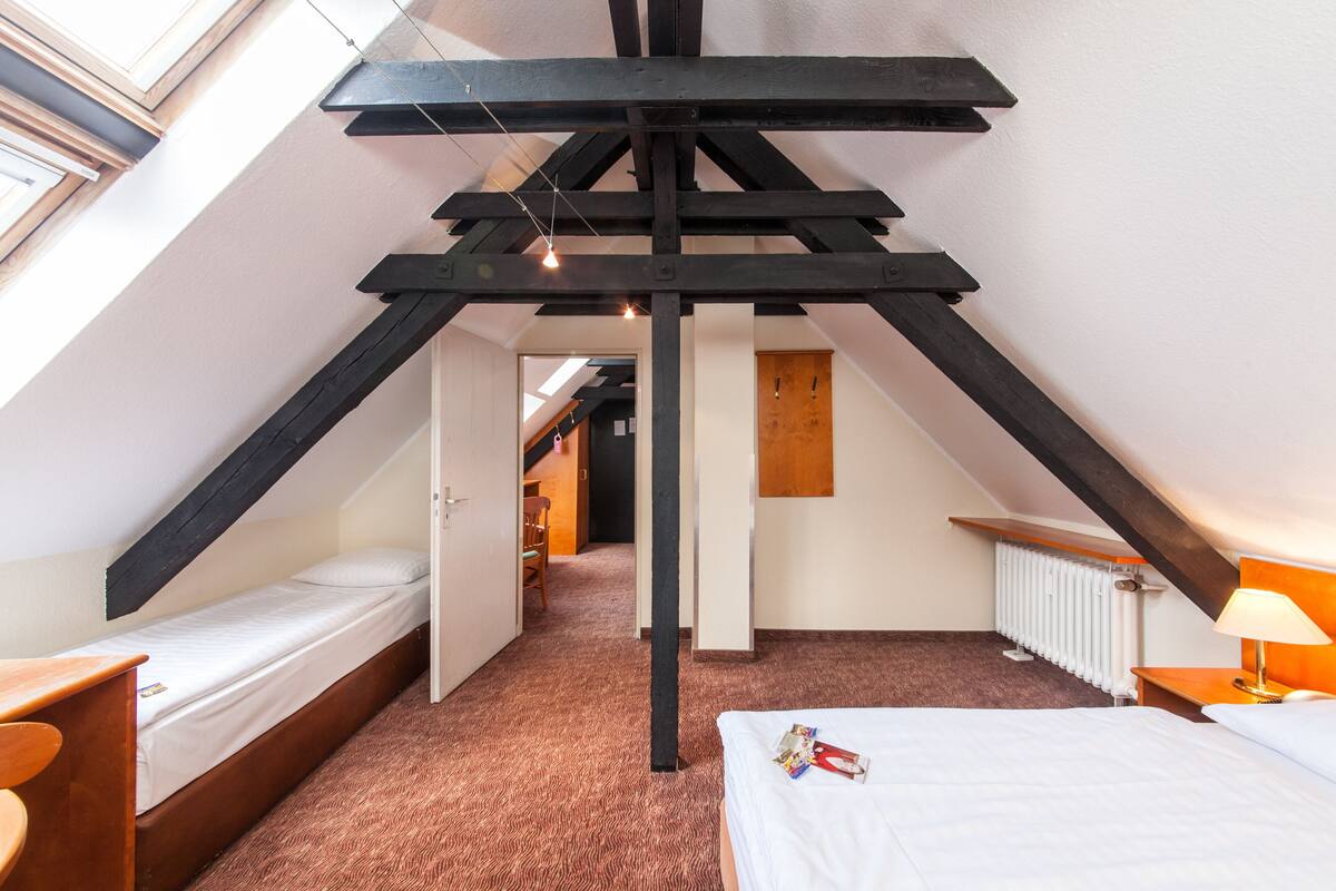 Een knus zolderkamertje met schuine wanden, een enkel bed, een bureau en een radiator.