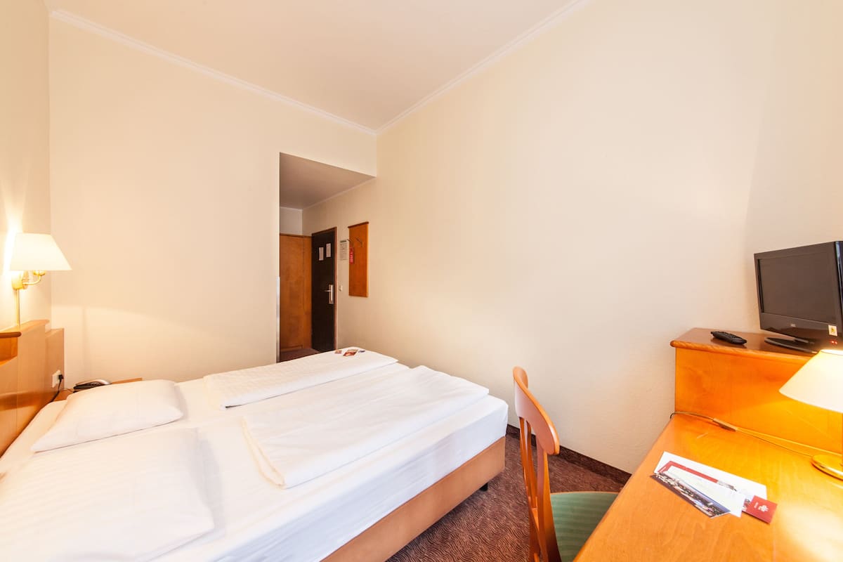 Een hotelkamer met een bed, een bureau met een lamp, een televisie en een deur die naar een andere kamer leidt.