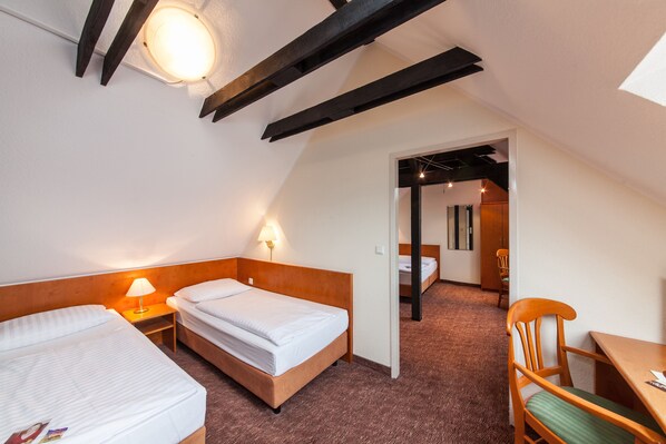 Une chambre d’hôtel avec deux lits, une table en bois, une chaise et un luminaire au plafond.