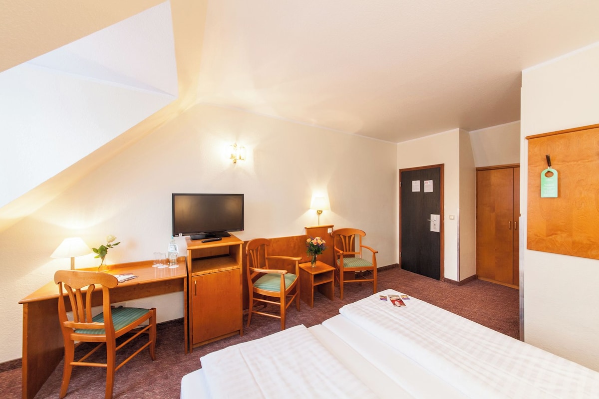 Een hotelkamer met een bureau, twee stoelen, een televisie, een bed en een deur.