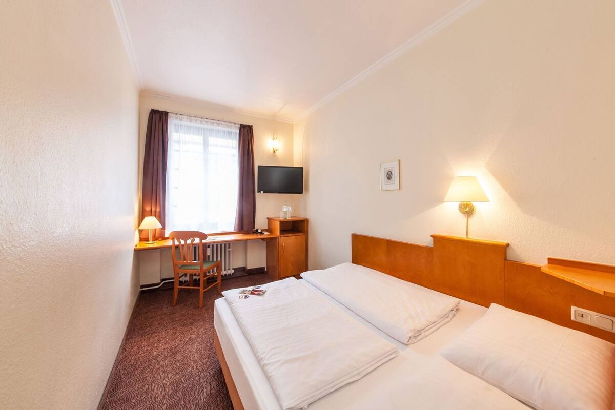 Een hotelkamer met een bed, bureau, stoel, televisie en een lamp.