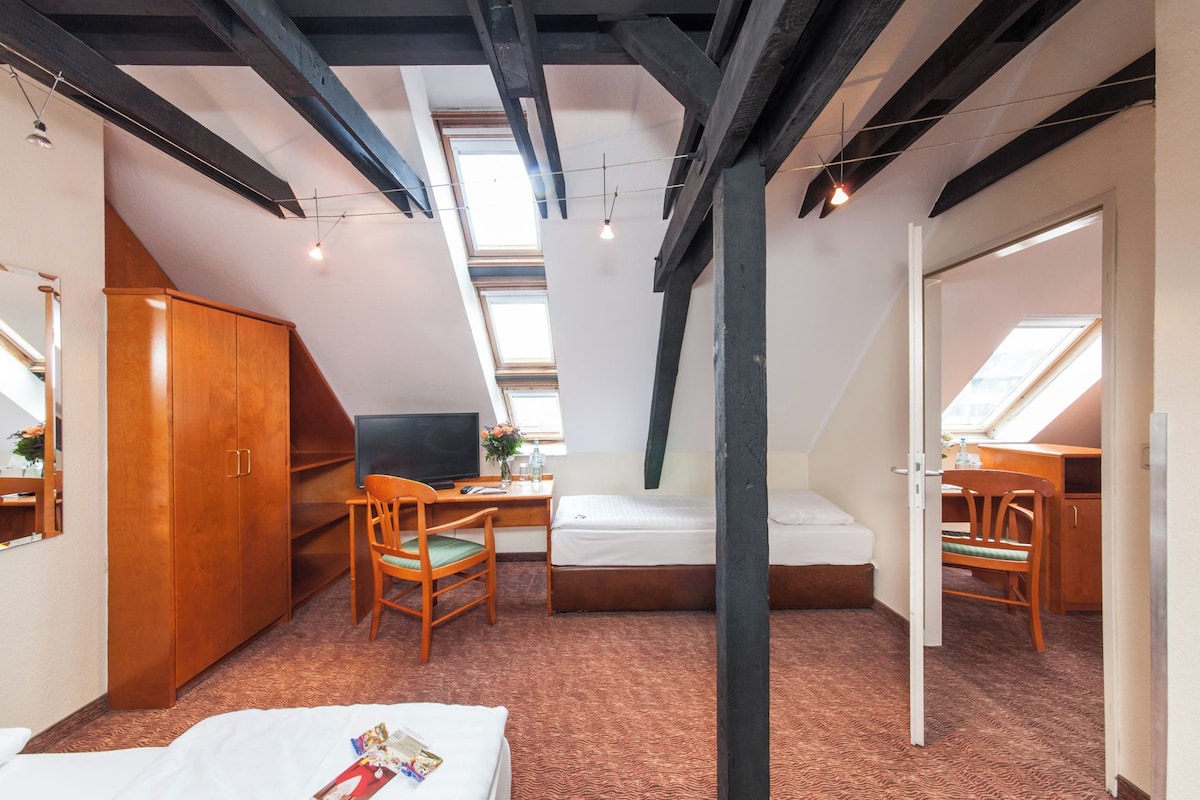 Een kleine kamer met een schuine kap, een bed, een bureau en een stoel.